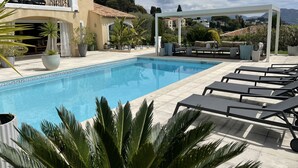 Et poolområde med liggestole, en pergola og udsigt over det omkringliggende landskab.