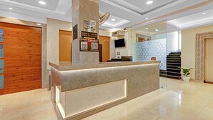 Un comptoir d’accueil d’hôtel avec un plan de travail en marbre, une porte en bois et un panneau indiquant les heures d’enregistrement.