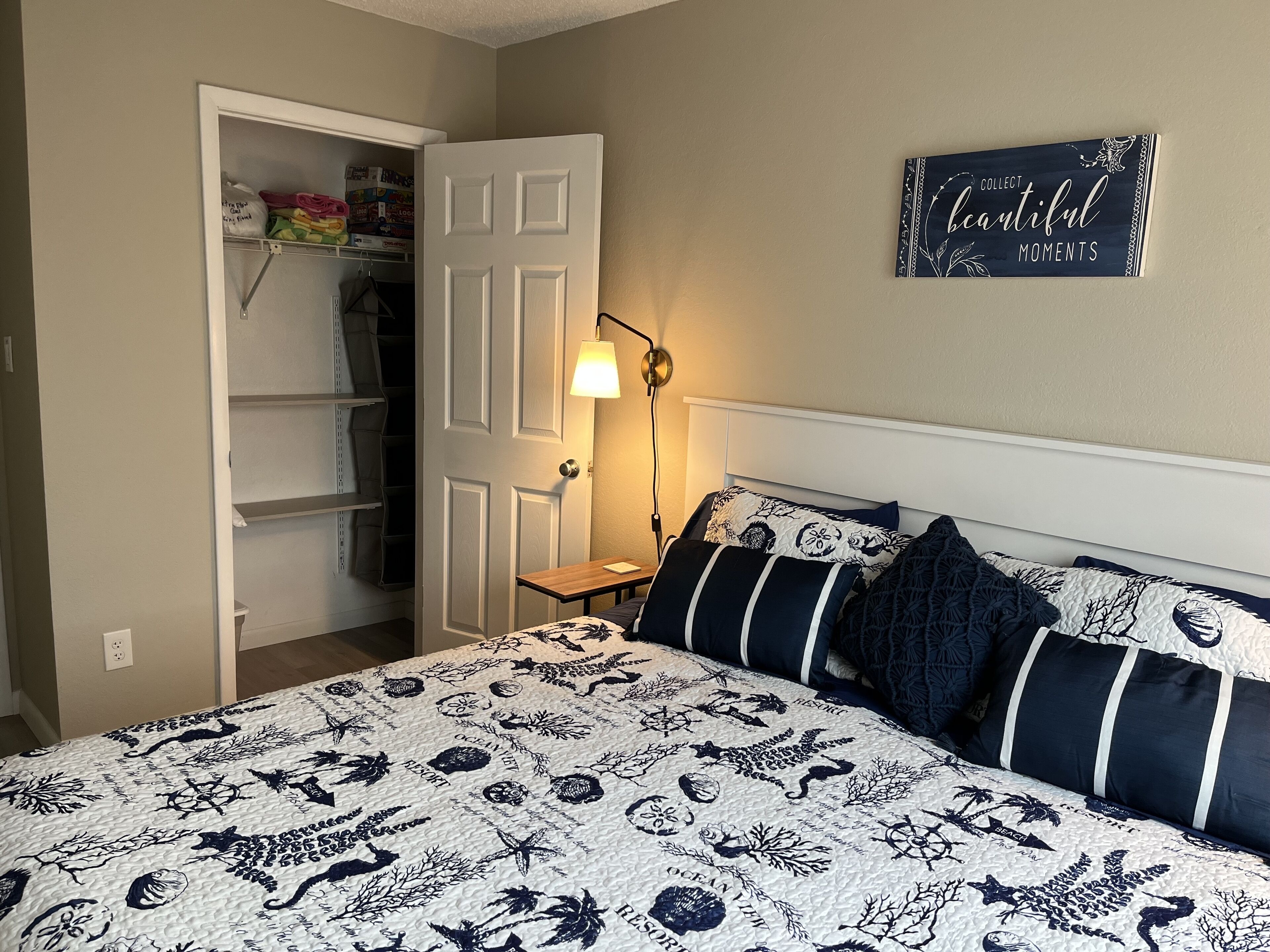 A bedroom with a bed, a nightstand, a lamp, a closet, and a wall sign.
