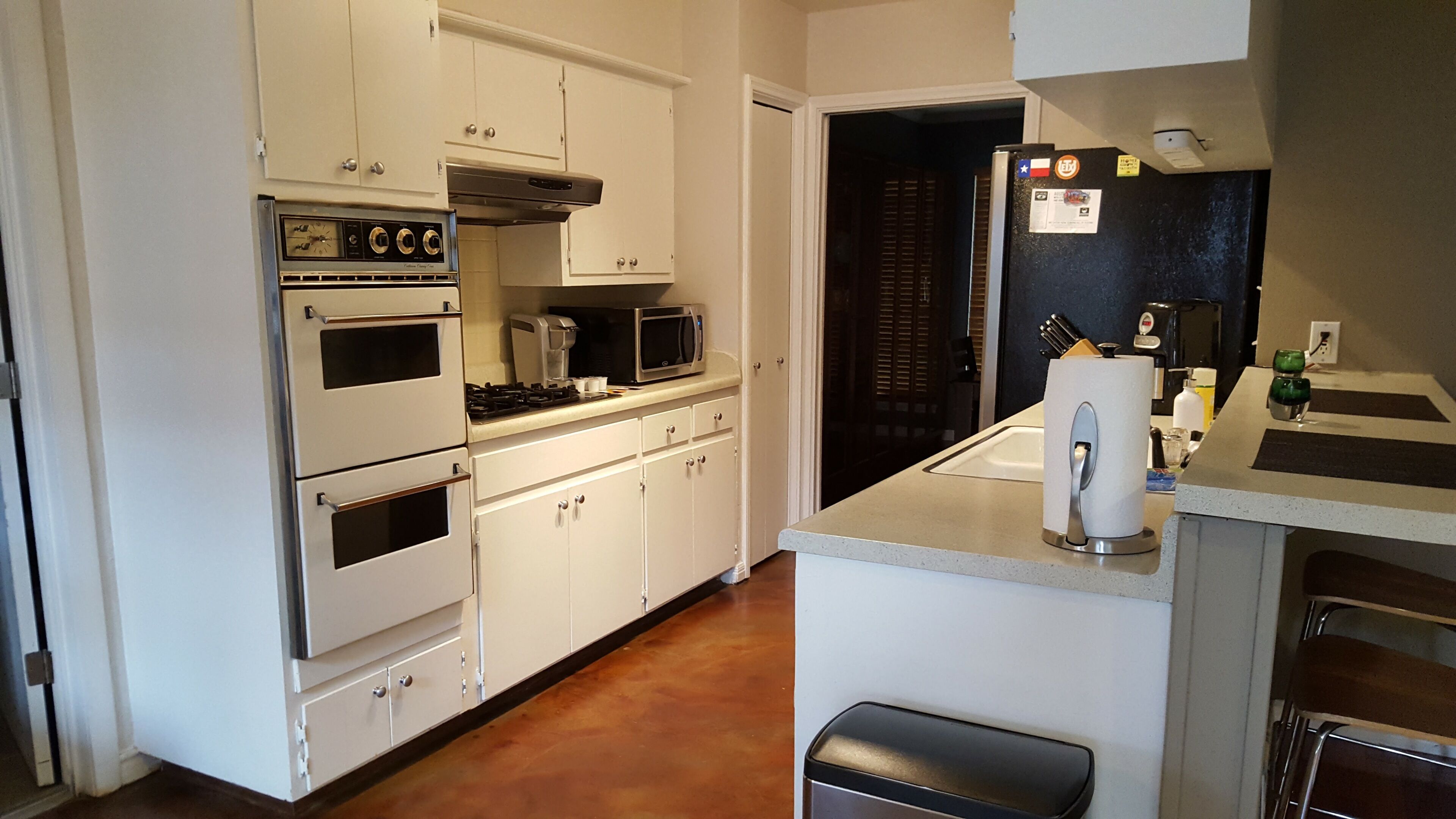 Una cocina con armarios blancos, estufa, microondas y pileta.