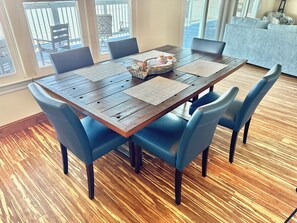 A dining area with a wooden table, blue chairs, and a view of the outside through large windows.
