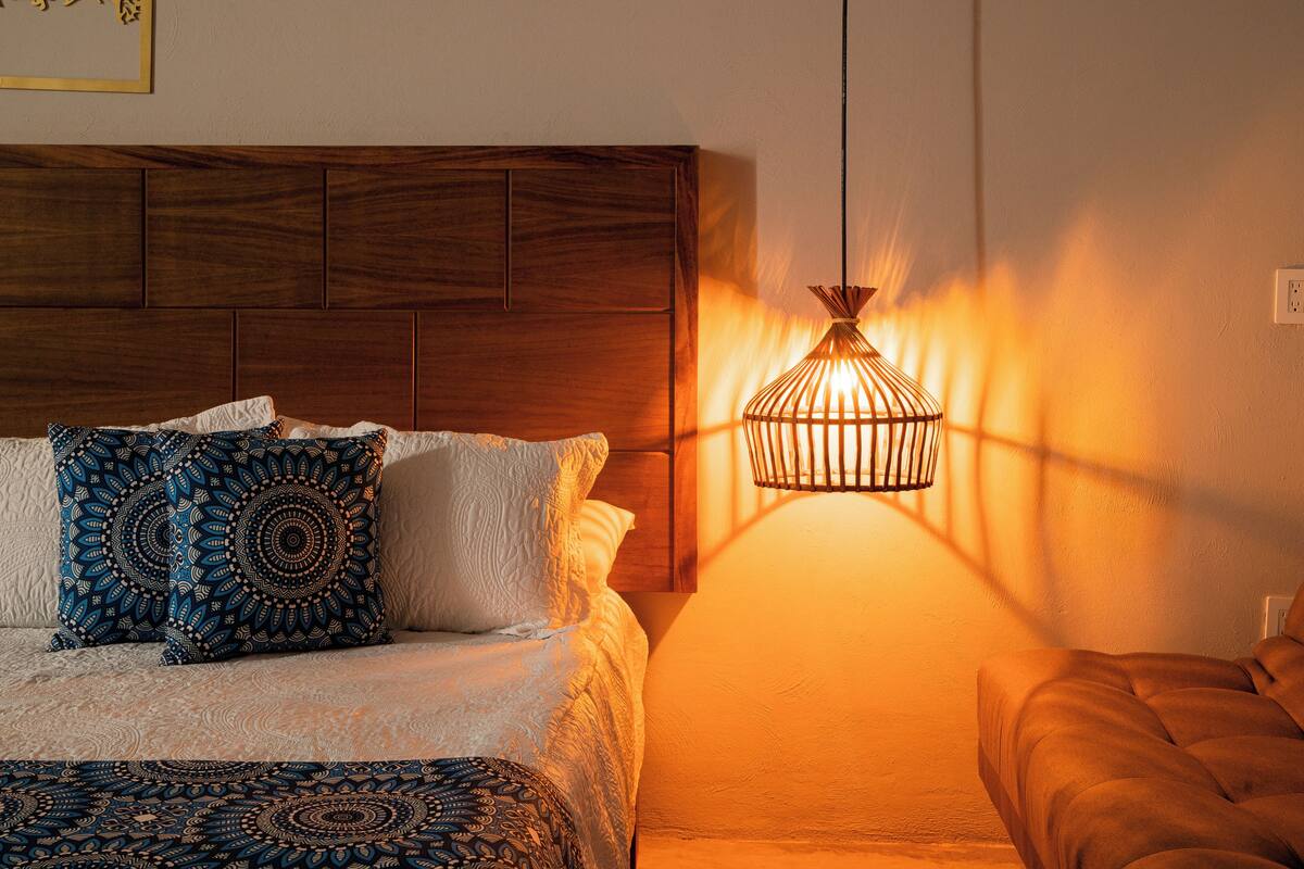Une chambre à coucher avec une tête de lit en bois, des coussins à motifs, une lampe de chevet et un banc rembourré.
