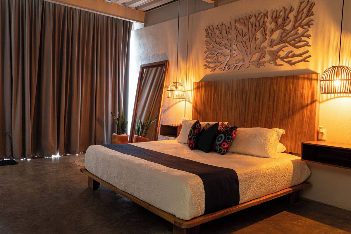 Une chambre à coucher avec un grand lit, une tête de lit en bois, des œuvres d’art murales et deux lampes de chevet.