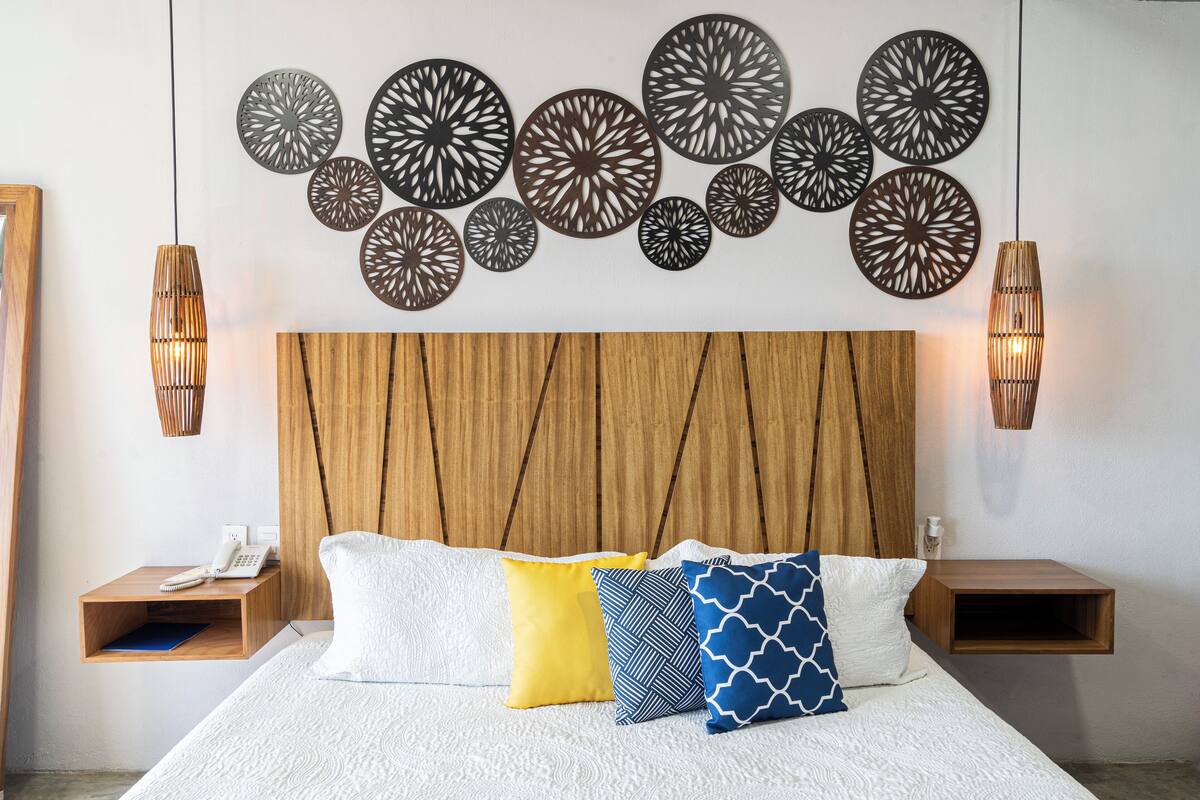 Une chambre à coucher bien aménagée, avec une tête de lit en bois, un lit recouvert de linge de lit blanc et des œuvres d’art décoratives accrochées au mur.