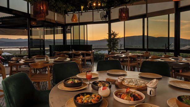 Een restaurant met uitzicht op de bergen, tafels gedekt met gerechten, en hangende lampen.
