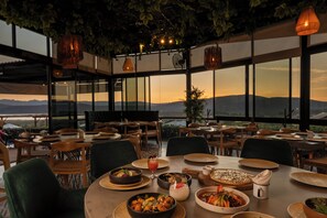 Un restaurant offrant une vue sur les montagnes, des tables dressées et décorées, et des luminaires suspendus.