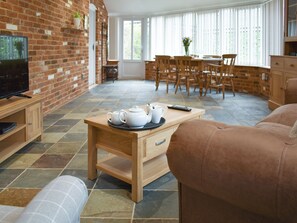 A cozy living room with a television, a coffee table with teapots, a sofa, and a dining area with chairs and a table.