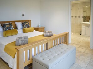 A bedroom with a bed, bedside tables, a bench, and a bathroom visible through an open door.