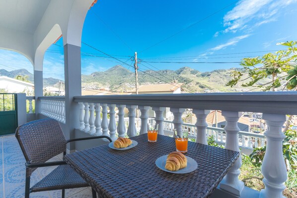 A balcony with wicker furniture, two croissants, and two glasses of orange juice.