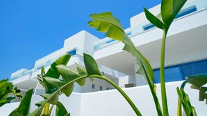 Un edificio moderno con fachada blanca y balcones, rodeado de exuberante vegetación.