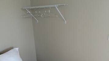 Una habitación de hotel con una cama, un almohadón blanco, un almohadón marrón y un tendedero metálico en la pared.