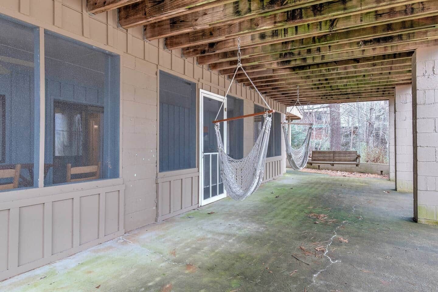 Eine überdachte Veranda mit einer Hängematte, einer Bank und Blick auf Bäume.
