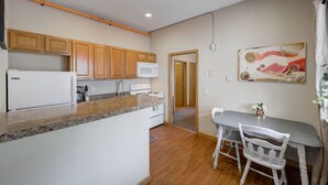 A kitchen with wooden cabinets, a microwave, and a dining area with a table and chairs. - Studio Condo Near Lake Pepin - King Bed - Dewdrop (Pepin)