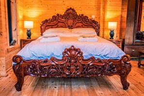 Ein großes, verziertes Bett aus Holz in einem Zimmer mit Holzwänden und Holzböden. Es gibt zwei Nachttische mit Lampen.