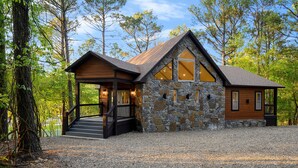 A rustic cabin with a stone exterior, wooden deck, and a large window. - Lakeside Cabin with Lots of Games! (Broken Bow)