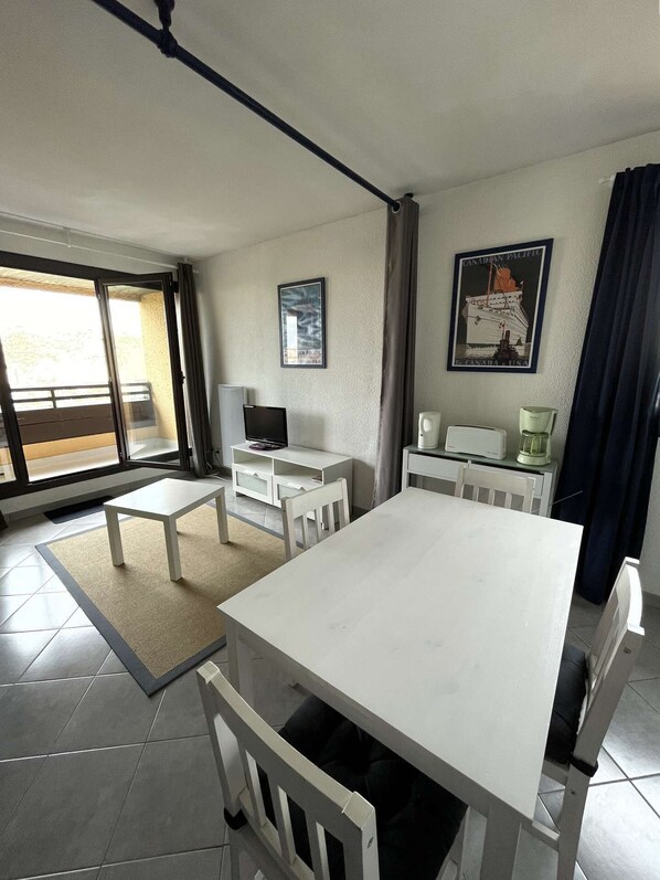 A modern, well-lit room with a large dining table, a television, and a coffee machine.