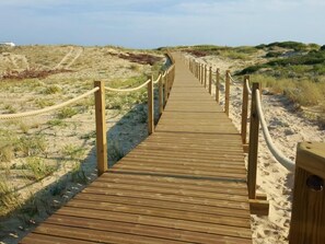 A wooden boardwalk leading through a sandy landscape with sparse vegetation.