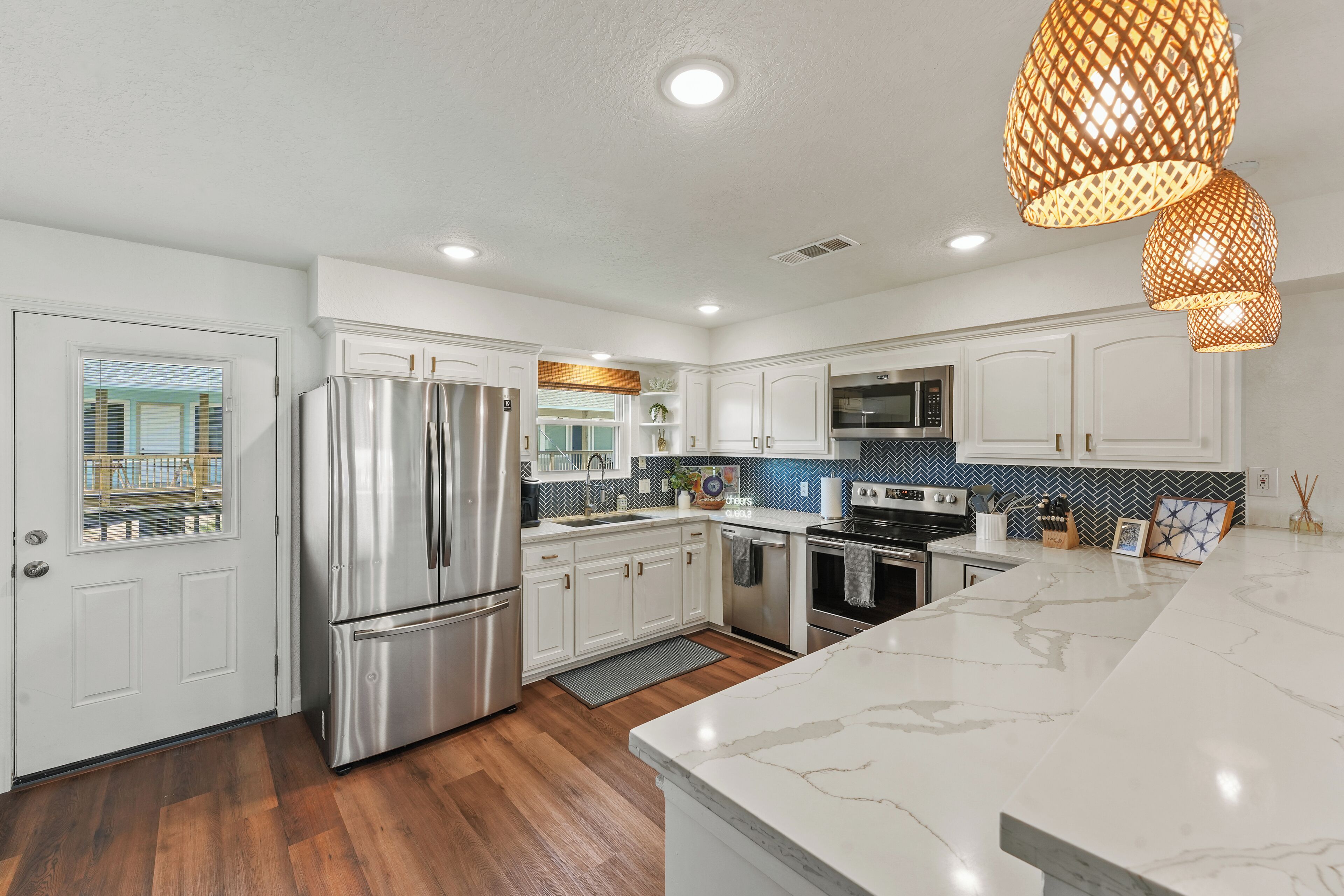 A modern kitchen with white cabinets, stainless steel appliances, a marble countertop, and pendant lighting.