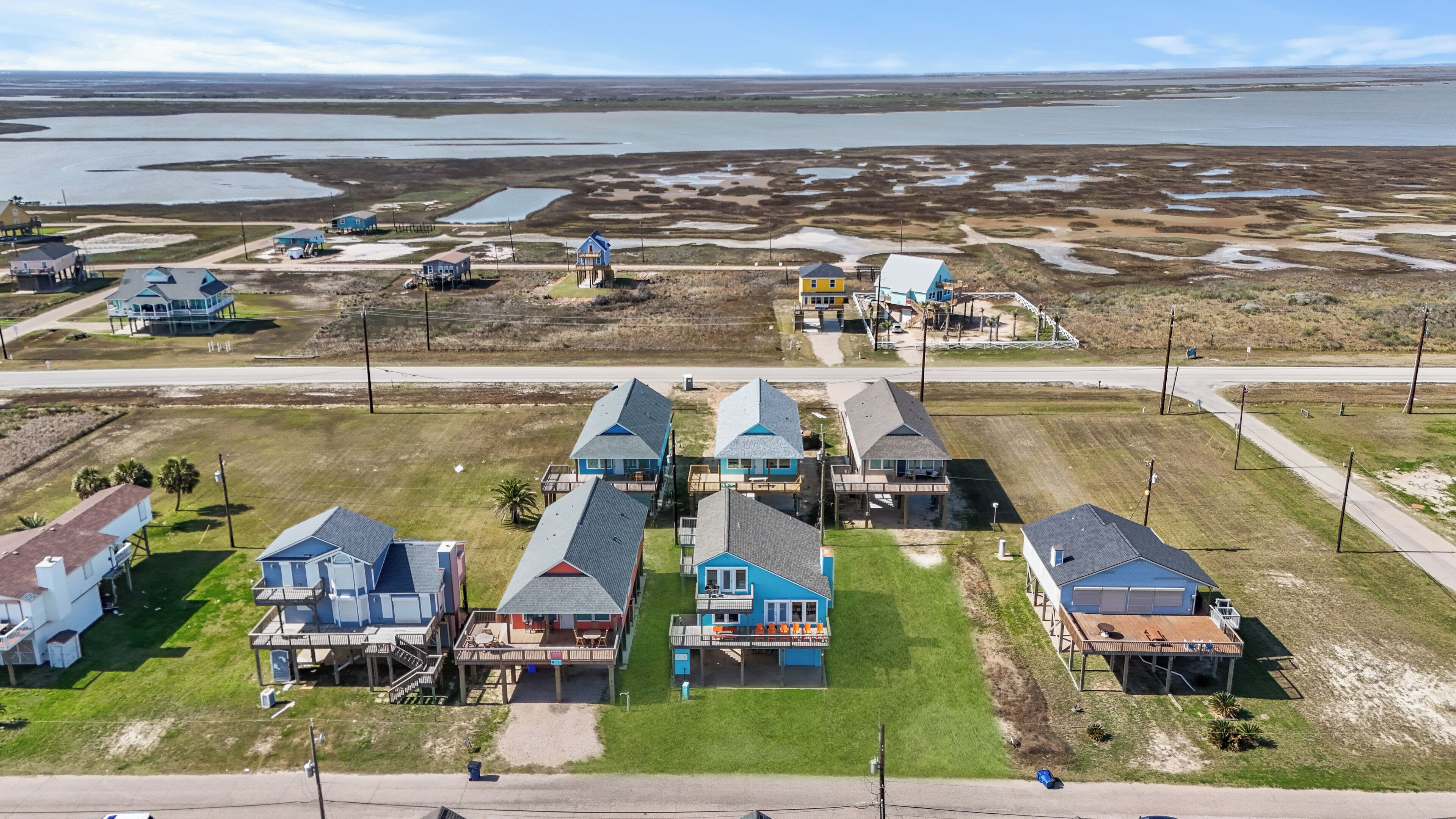 Vista aérea de una zona residencial costera con casas de varios pisos y balcones, una carretera y una gran masa de agua al fondo.