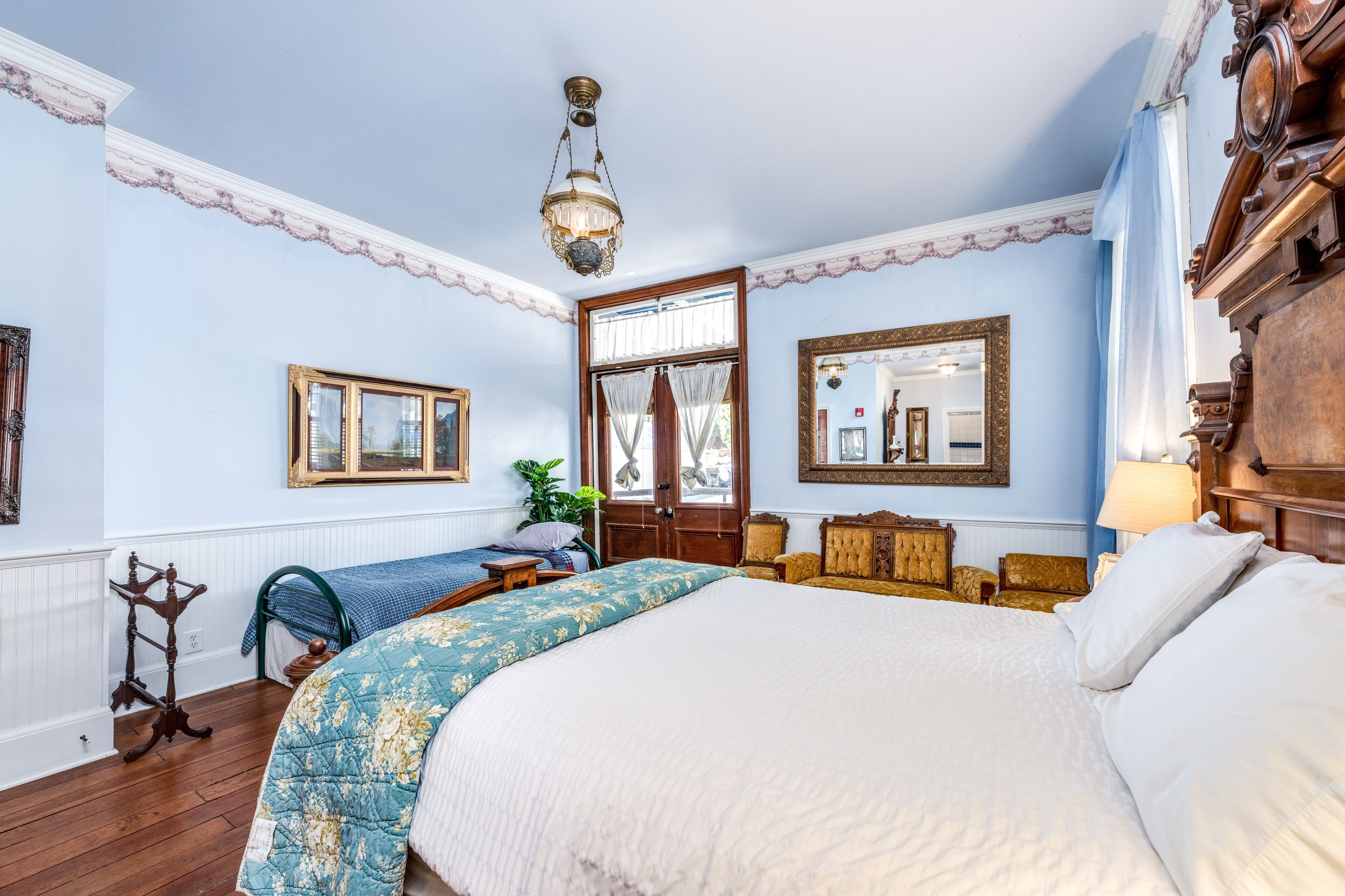A bedroom with a large bed, a wooden dresser, a mirror, and a window with curtains.