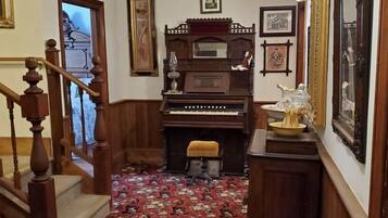 Un passadís amb una escala de fusta, un piano i una catifes amb motius florals.