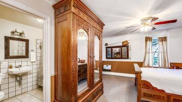 A bedroom with a wooden bed, a ceiling fan, a large mirror, and a bathroom with a sink and toilet.