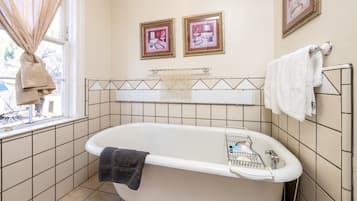 A bathroom with a bathtub, a window with curtains, and two framed pictures on the wall.