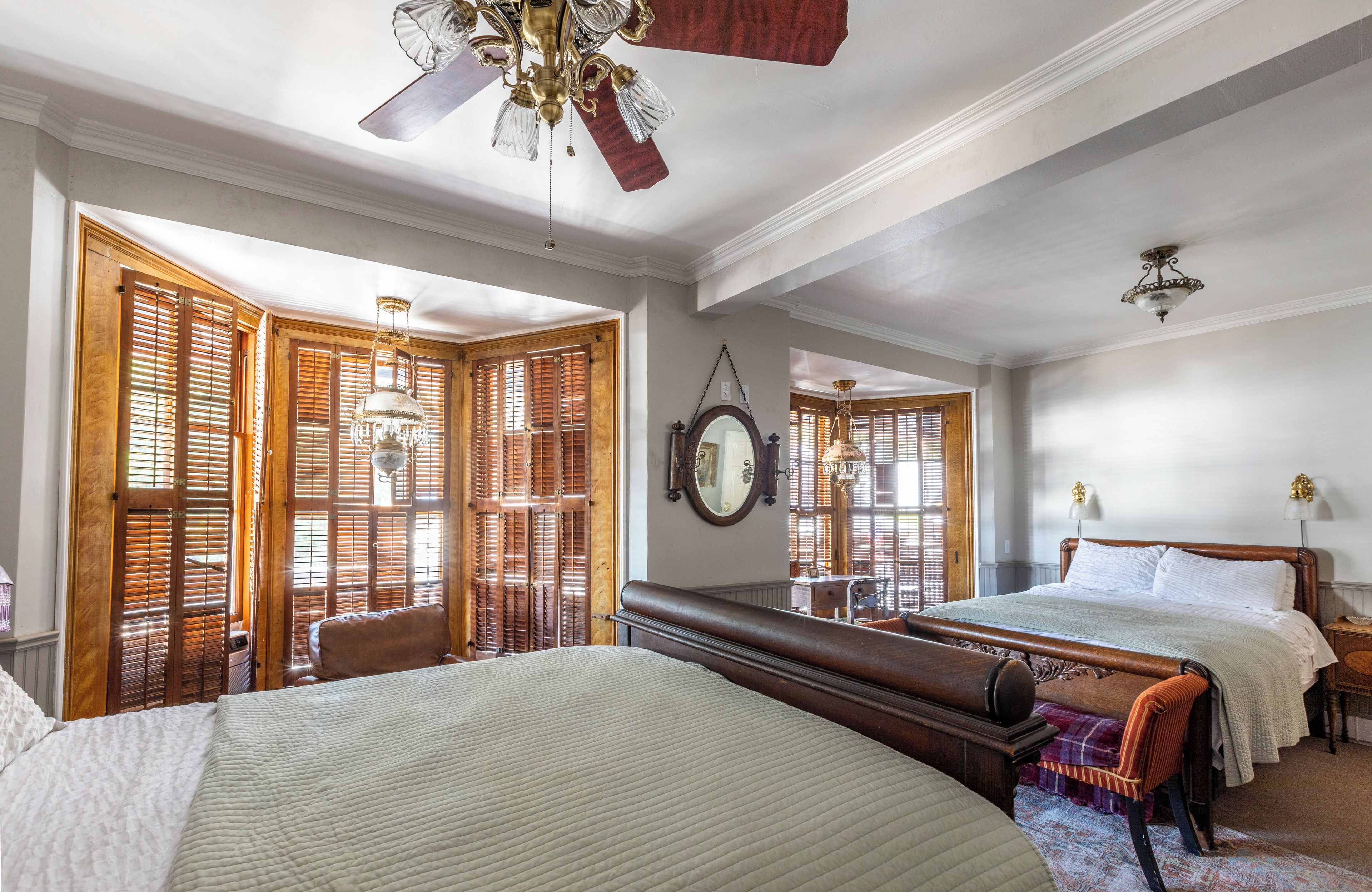 A bedroom with a large bed, a smaller bed, a chair, a desk, and a ceiling fan.