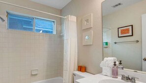 Ein Badezimmer mit einer Badewanne, Toilette, Waschbecken, Fenster und Spiegel.