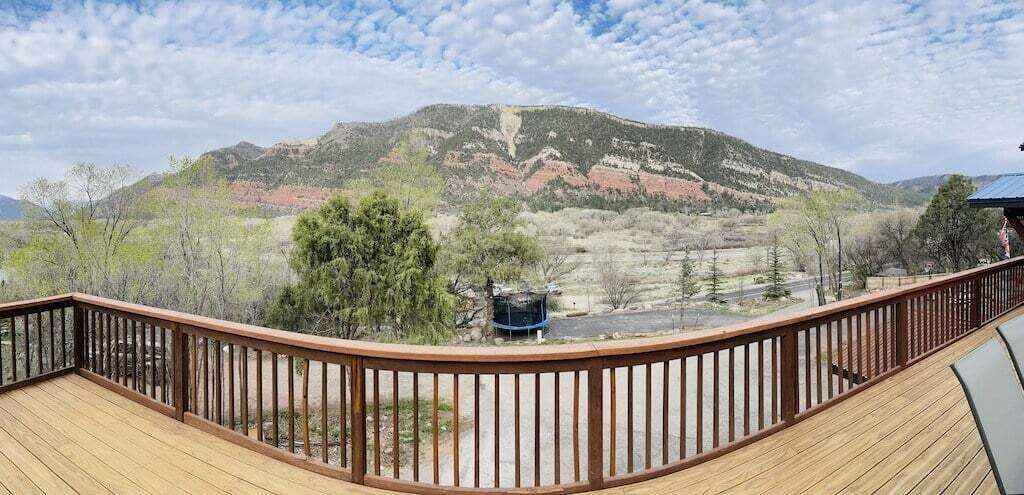 A wooden deck with a metal railing overlooking a mountainous landscape.