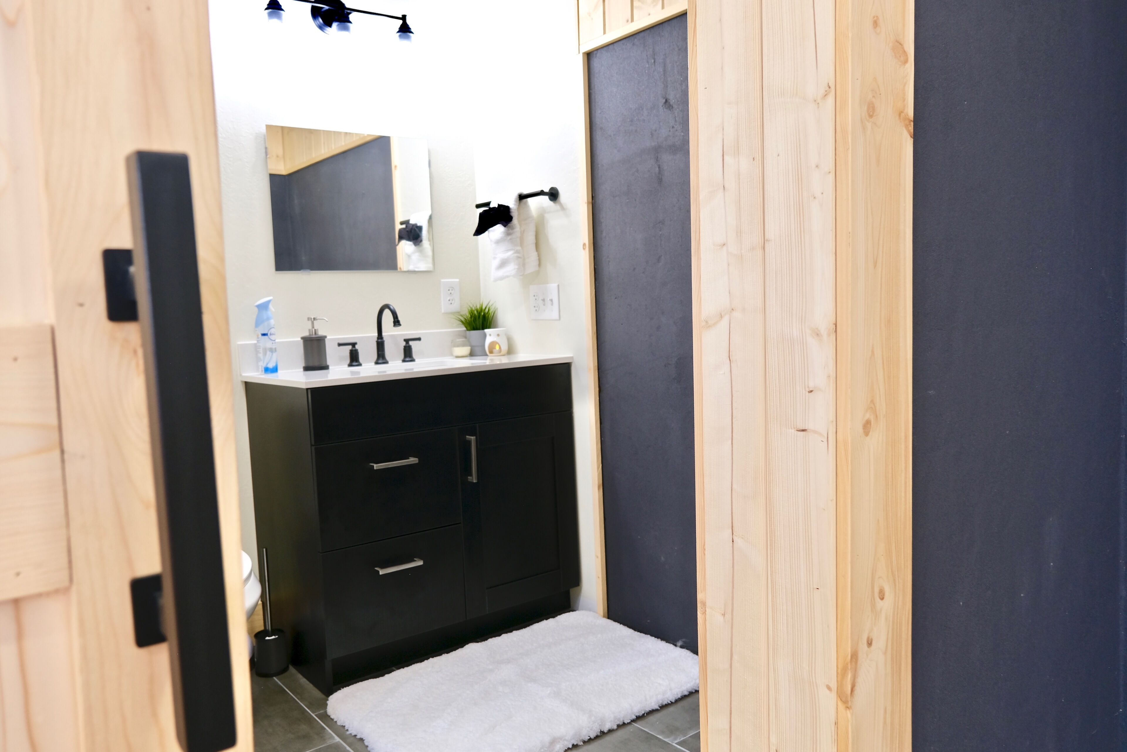 A bathroom with a wooden door, a white sink with a black faucet, a small mirror, and a white towel hanging on the wall.