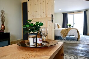 Quarto de hotel com mesa de madeira, garrafa de vinho rosé, um copo e um vaso com planta.