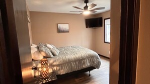 Quarto com cama, ventilador de teto, TV na parede e janela.