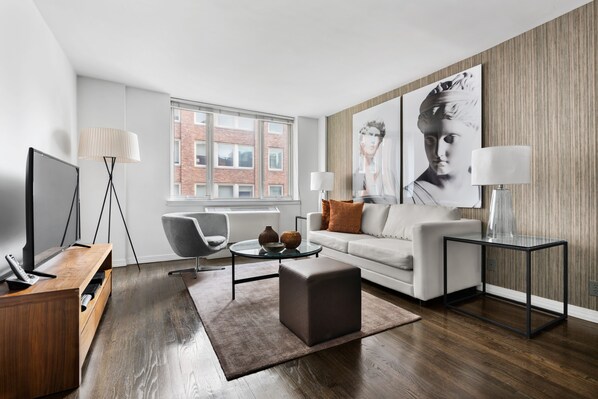 A modern living room with a flat-screen TV, a coffee table, a sofa, and a side table with lamps.