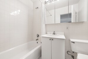 A modern bathroom with white tiles, a bathtub, a sink, and a toilet.