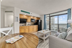 Enjoy ocean views from the balcony, which offers a chair and a table. The compact living space features a kitchenette with a microwave and refrigerator, and a cozy seating area with a sofa.