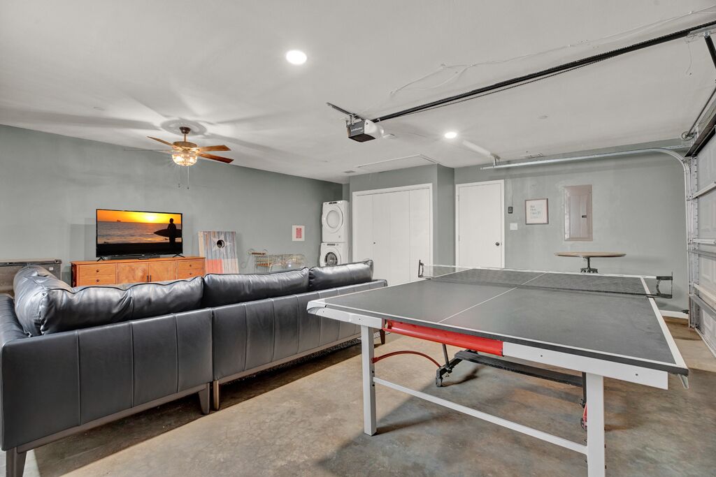A room with a ping pong table, a leather couch, a TV, and a ceiling fan.