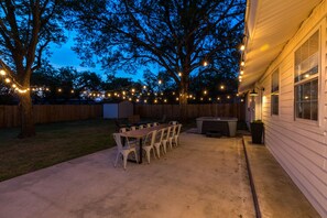 A backyard patio with a table and chairs, surrounded by a wooden fence and trees. - Fall Wine Escape - Walk to Main - GameRm + Hot Tub (Fredericksburg)
