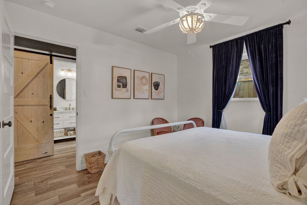 Un dormitorio con cama, ventilador de techo, ventana con cortinas y puerta que da a un baño.