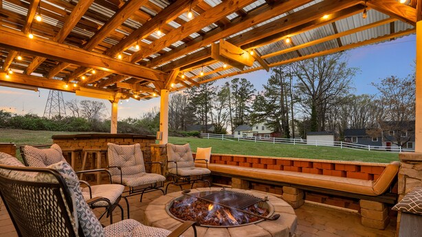 An outdoor patio with a fire pit, seating, and a view of a grassy field and houses. - Bright & Spacious Studio Close To CLT Airport & Charlotte (Gastonia)
