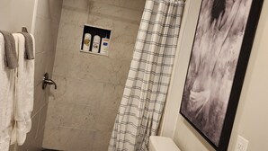 A bathroom with a shower, toilet, and sink. There is a towel rack with towels, a shower curtain, and a framed picture on the wall. - Bright & Spacious Studio Close To CLT Airport & Charlotte (Gastonia)
