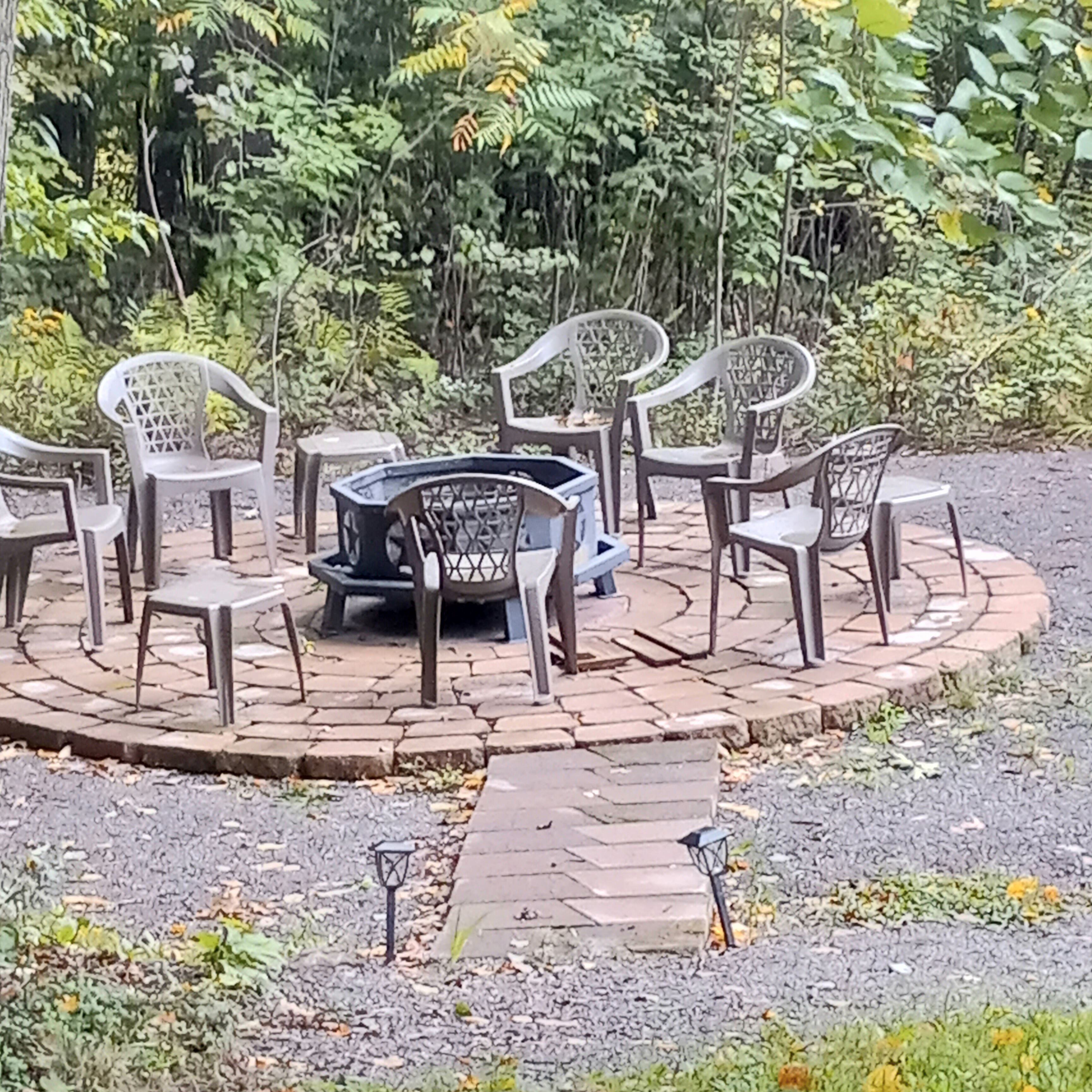A circular outdoor seating area with plastic chairs and a central table, surrounded by a brick pathway.