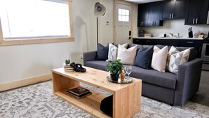 A modern living room with a grey sofa, a wooden coffee table, and a patterned rug.