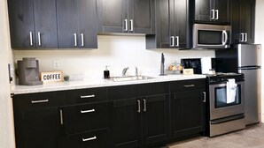 A modern kitchen with dark cabinetry, a stainless steel refrigerator, a microwave, and a coffee maker.
