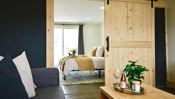 A modern living room with a sofa, a coffee table with a tray of items, and a view into a bedroom with a bed and a sliding door.