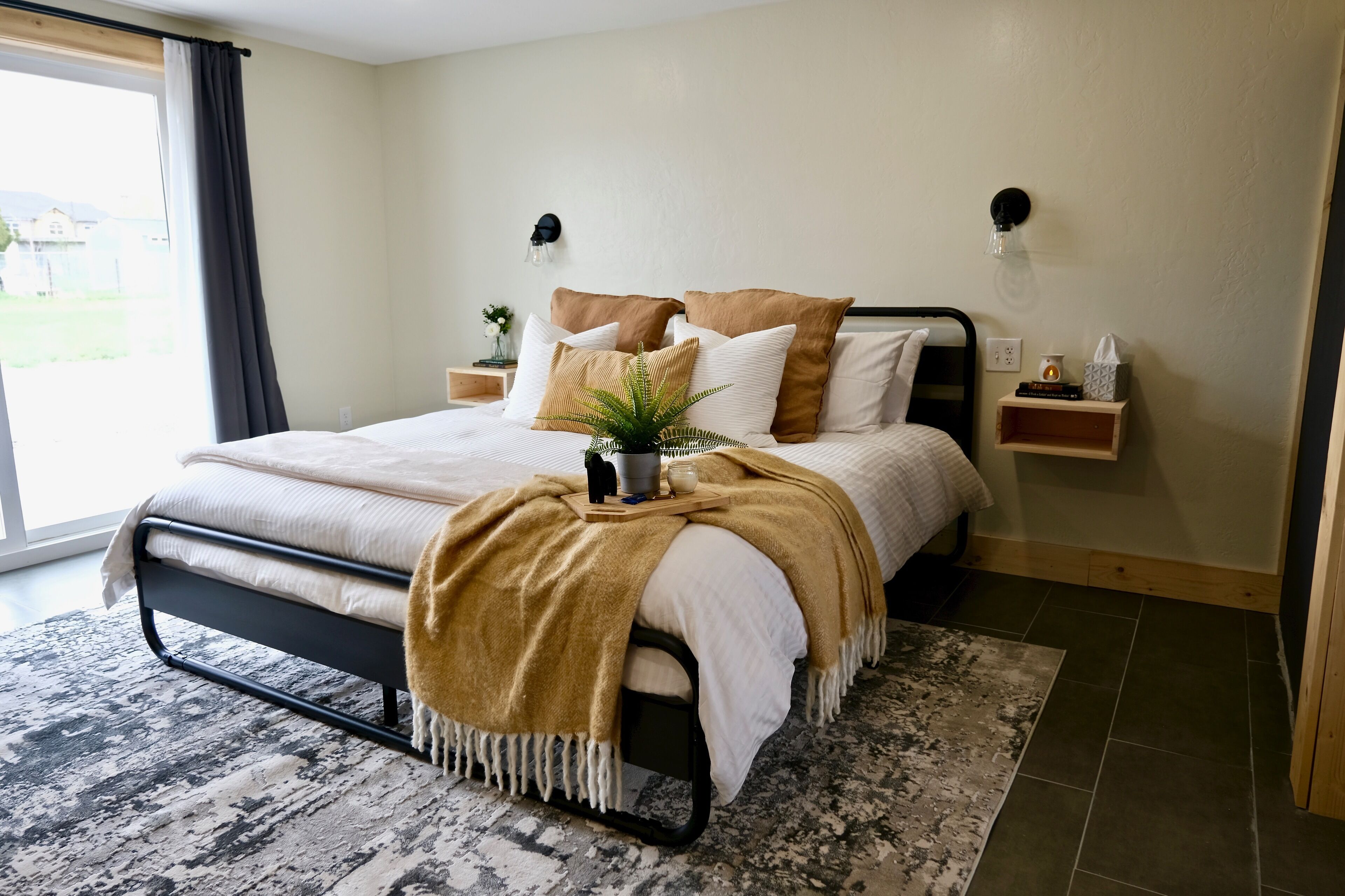 Une chambre à coucher avec un lit, des tables de chevet, une commode, une fenêtre avec des rideaux et une vue sur l’extérieur.