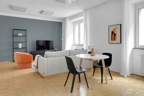 Relax in this stylish living room with a sofa, round table, and TV, surrounded by a large window and a beautiful abstract art piece.