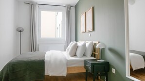 Une chambre à coucher avec un lit, une table de chevet avec une lampe, une fenêtre avec des rideaux et un miroir sur le mur.