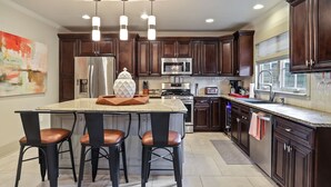 A modern kitchen with dark wood cabinets, stainless steel appliances, and a central island with bar stools. - The Garden District Retreat - close to everything! (Baton Rouge)