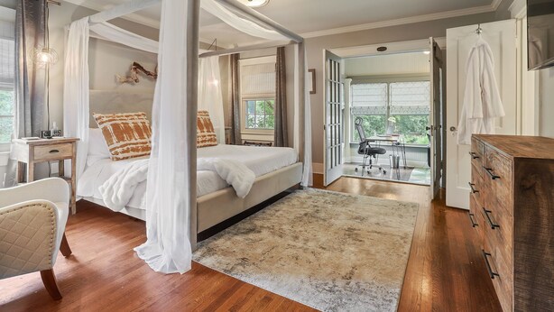 A bedroom with a four-poster bed, a wooden dresser, a chair, and a view of the outdoors. - The Garden District Retreat - close to everything! (Baton Rouge)